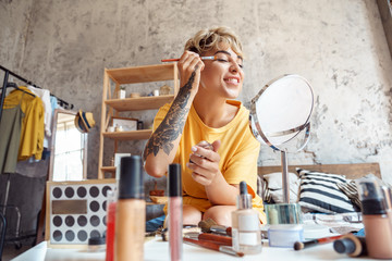 Make-up Blogger. Young woman sitting at stylish apartment applying eyeshadow looking at mirror...