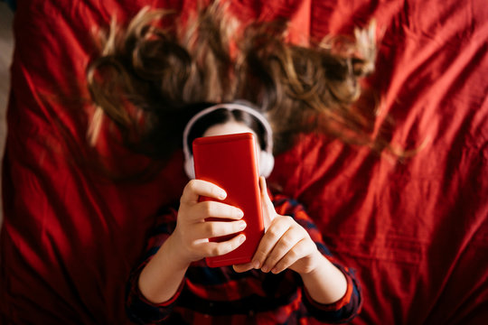 Girl using mobile phone in bedroom for making portrait and sending virtual messages for friends. Valentine's day concept. Top view gadget covering face. Faceless concept