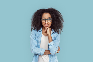 Fototapeta premium Freestyle. African girl in glasses standing isolated on gray touching chin curious
