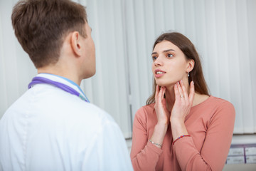 Young woman with sore throat visiting doctor. Female patient with seasonal flu on medical appointment at the hospital