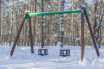 The empty childrens swing on a playground in a snowy winter park.