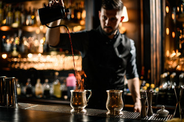 Male bartender pours alcohol from kettle to cup