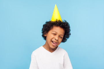 Portrait of humorous funny naughty little boy with party cone on head sticking out tongue and...