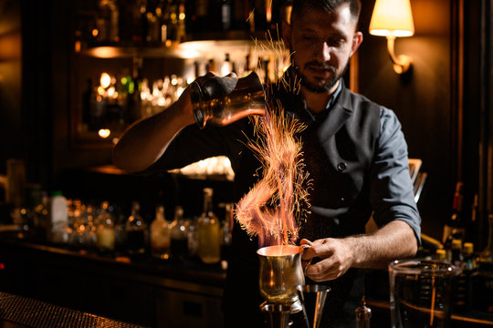 Male bartender flows burning liquid from mug to mug
