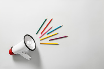 Megaphone with colorful pencils on white background