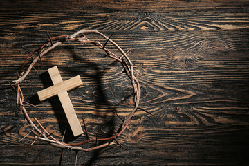 Wreath of thornes and cross on wooden background