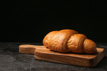 Board with tasty croissant on dark background