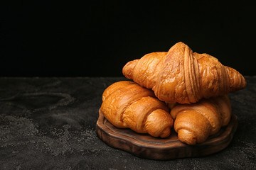 Board with tasty croissants on dark background