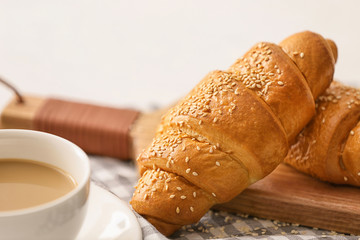 Board with tasty croissants and cup of coffee on table