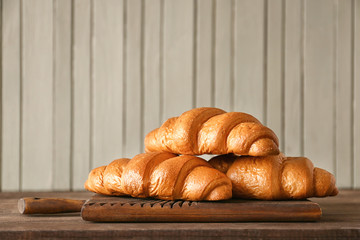 Board with tasty croissants on wooden table