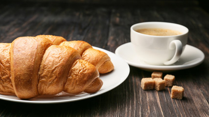 Plate with tasty croissants and cup of coffee on table