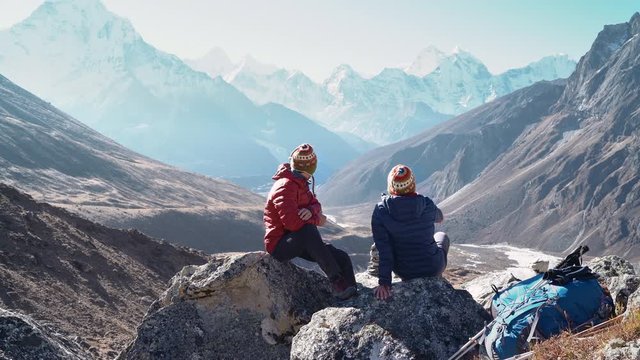 4K footage of Young Couple sitting on stones, speaking, resting on the Everest Base Camp trekking route near Dughla 4620m. They left Backpacks and trekking poles and enjoying valley view with Ama Dabl