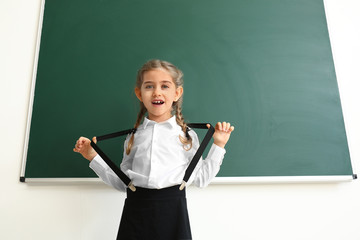 Little schoolgirl near blackboard in classroom