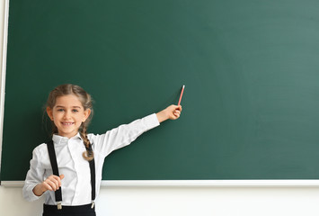 Little schoolgirl near blackboard in classroom