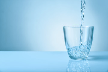 Pouring of fresh water into glass on color background