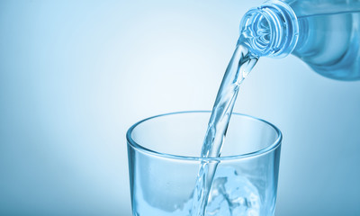 Pouring of fresh water into glass on color background