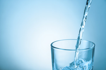 Pouring of fresh water into glass on color background
