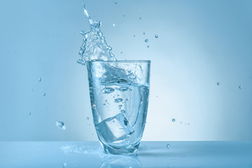Glass of fresh water with splash on color background