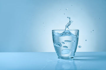 Glass of fresh water with splash on color background