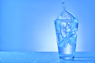 Glass of fresh water with splash on color background