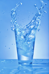 Glass of fresh water with splash on color background