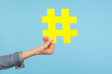 Closeup of yellow hash sign, female hand holding paper hashtag, symbol of social network trends and popular comments, famous blog content, promotion. indoor studio shot isolated on blue background