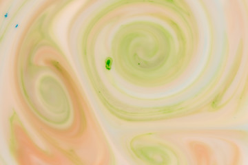 Green and orange swirls in white liquid. Abstract background from dissolving paints.