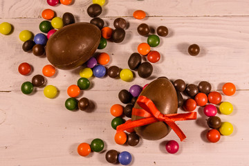 Chocolate easter eggs and multicolored candies on wooden table. Top view