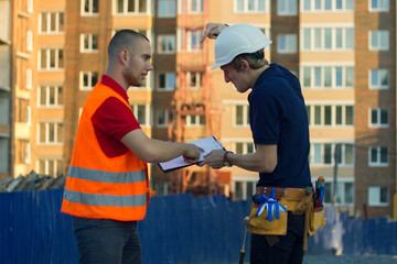Fototapeta premium Two engineer builders with blueprint plan at construction site