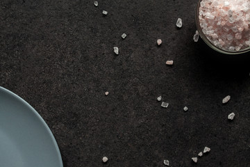 A gray plate and sprinkled Himalayan salt on a dark table.