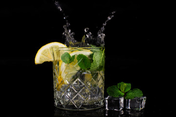  mojito cocktail drink with mint and lemon lime in a glass splash splashing out of a glass with ice cubes, drops and splashes on a black background