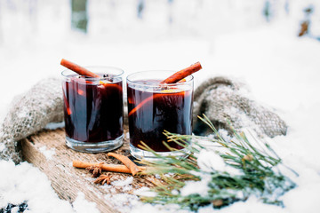Mulled wine on a wooden board on a snowy table. Two glasses of hot wine with cinnamon and fresh...