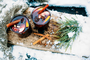 Mulled wine on a wooden board on a snowy table. Two glasses of hot wine with cinnamon and fresh...