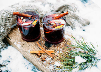 Mulled wine on a wooden board on a snowy table. Two glasses of hot wine with cinnamon and fresh...