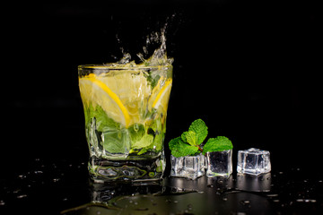  mojito cocktail drink with mint and lemon lime in a glass splash splashing out of a glass with ice cubes, drops and splashes on a black background