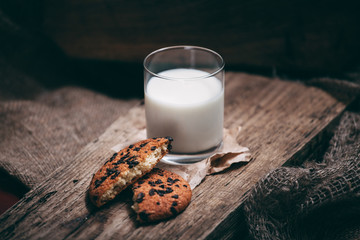 Cookies with pieces of chocolate and milk on a wooden stand with a cloth on the sides.