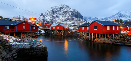 Small fishing village of A (Moskenes) at the end of the road of the Lofoten islands archipelago in northern Norway - Red rorbuer on stilts in winter at dawn in a fjord