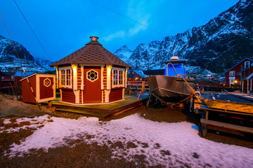 Wooden sauna house in the small fishing village of A (Moskenes) at the end of the road of the Lofoten islands archipelago in northern Norway - Red rorbuer on stilts in winter at dawn in a fjord