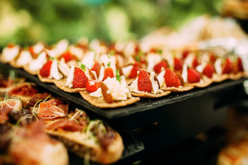 Sweet canapes with cream cheese and strawberries. Food table at an open-air party.