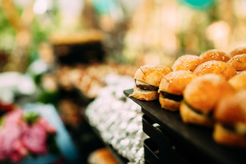Mini burgers and canapes on the festive table. Beautifully decorated grass and flowers table with food at an open-air party