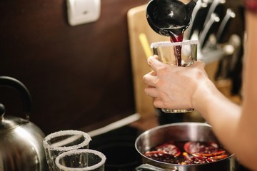Girl pours hot mulled wine into glasses. The edges of the glasses are coated with sugar.