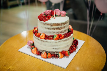 Big cake decorated with berries and flowers with a first birthday candle