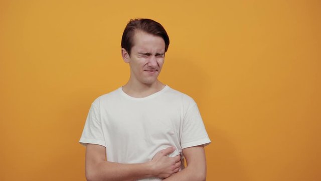 Man in a white t-shirt with abdominal pain health problem discomfort diarrhea yellow background