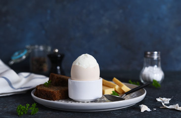 Classic breakfast - soft-boiled egg with whole grain bread on a dark background.
