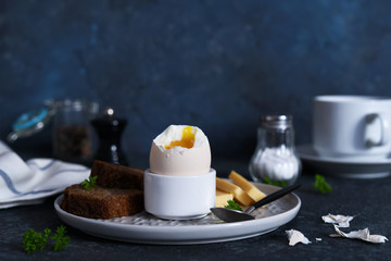 Classic breakfast - soft-boiled egg with whole grain bread on a dark background.