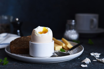 Classic breakfast - soft-boiled egg with whole grain bread on a dark background.