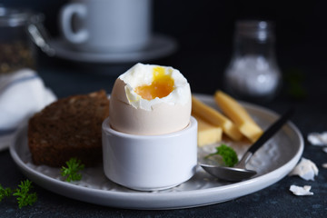 Classic breakfast - soft-boiled egg with whole grain bread on a dark background.