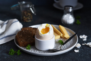 Classic breakfast - soft-boiled egg with whole grain bread on a dark background.