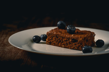 Selbstgebackene Brownies mit Heidelbeeren auf einem weissen Teller, mit dunklen Hintergrund