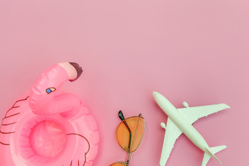 Summer beach composition. Minimal simple flat lay with plane sunglasses and Inflatable flamingo isolated on pastel pink background. Vacation travel adventure trip concept. Top view copy space.